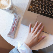 Cafebord med dator och en latte med en hand från en kvinna som stäcker sig efter sitt järnrika mellanmål som är en hemjärnsbar